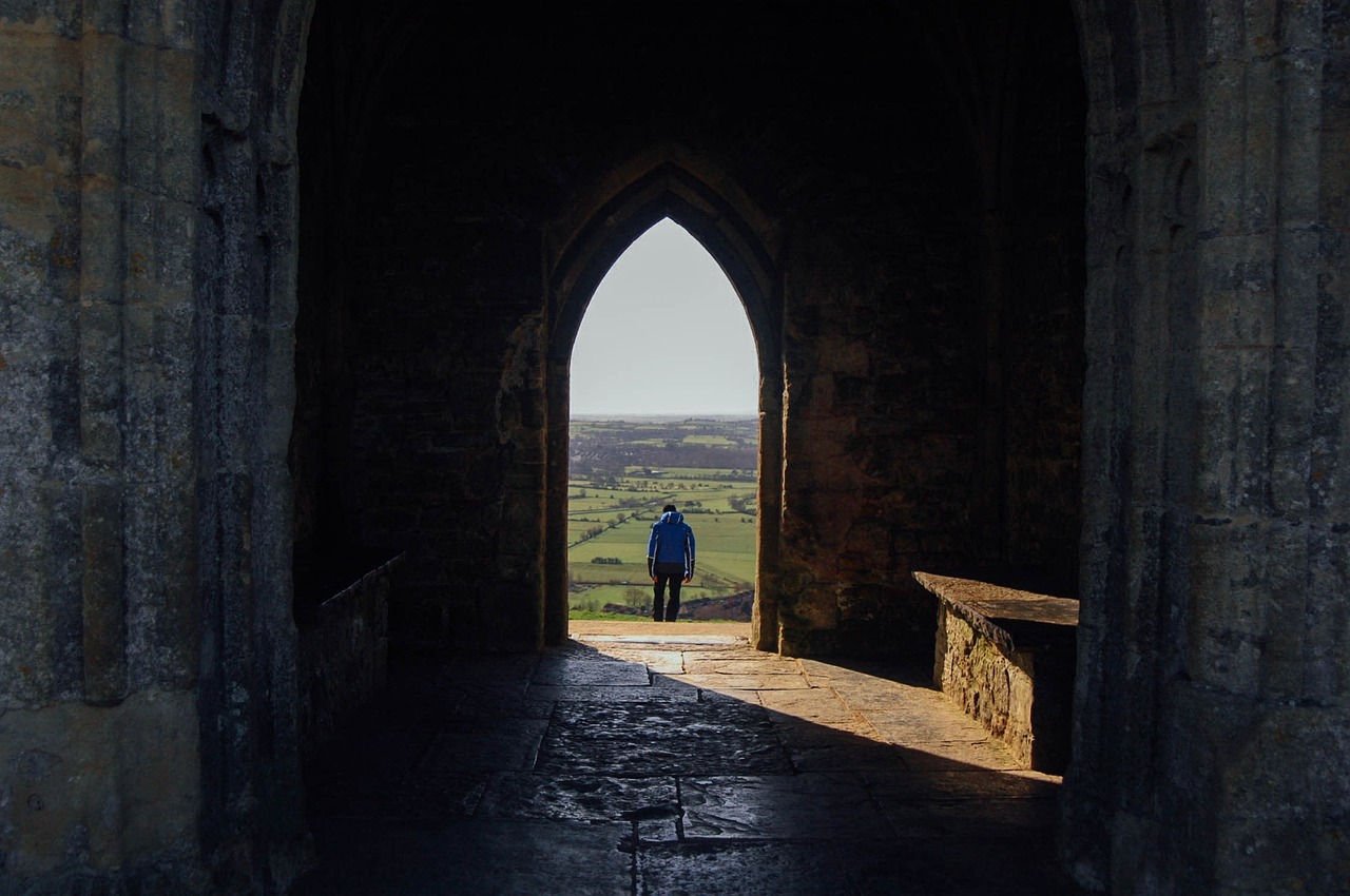 A young man standing in the door of an old church looking out at the surrounding countryside